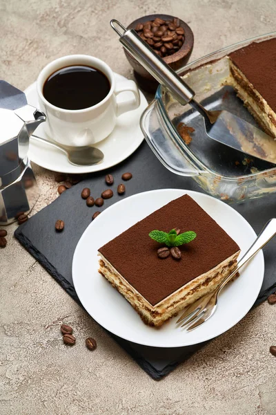 Традиционный итальянский десерт Tiramisu в стеклянной выпечке и порция на сером бетонном фоне — стоковое фото