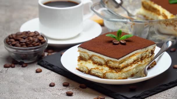 Traditionelles italienisches Tiramisu-Dessert in Glasauflaufform und Portion auf grauem Betongrund — Stockvideo