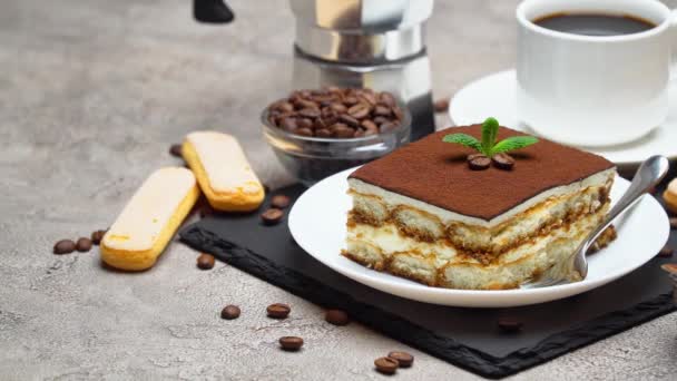 Portion of Traditional Italian Tiramisu dessert and mocha coffee maker on grey concrete background — Stock Video