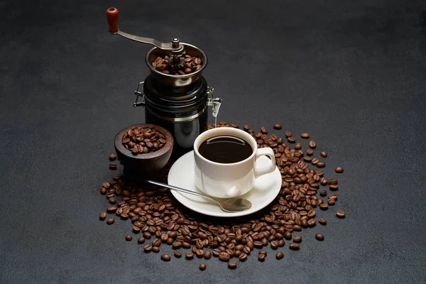 Copa de café expreso y molinillo de mano en granos de café marrón tostado sobre fondo de hormigón —  Fotos de Stock