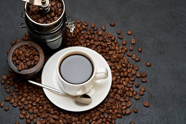 Filiżanka kawy espresso i szlifierka do rąk na palonej brązowej ziarnie kawy na betonowym tle — Zdjęcie stockowe