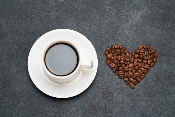 Kopje espresso en hartvormige gebrande koffiebonen op donkere betonnen achtergrond — Stockfoto
