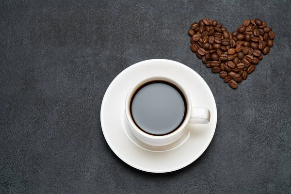 Kupa eszpresszó és szív alakú pörkölt kávébab sötét beton alapon — Stock Fotó