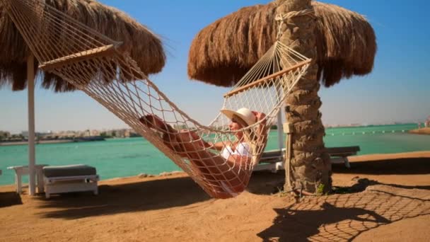 Концепция путешествий и отдыха - Женщина отдыхает на гамаке на пляже — стоковое видео