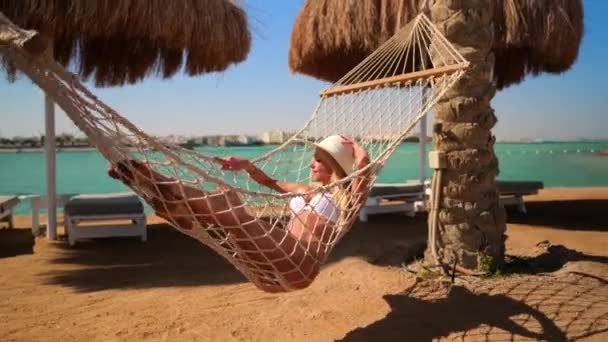 Концепція подорожей та відпусток - жінка відпочиває на гамаку на пляжі — стокове відео