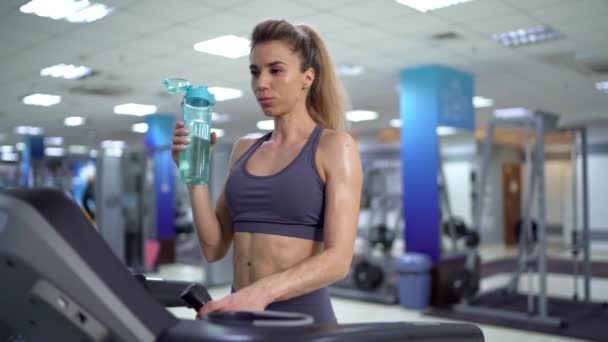 Ung sportig kvinna på löpning maskin i gym dricksvatten — Stockvideo