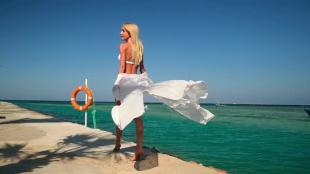 Mooie jonge vrouw in wit pareo staan op pier in de buurt van zee — Stockvideo