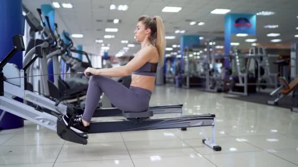 Młoda kobieta ćwiczy na maszynie rzędowej na siłowni — Wideo stockowe