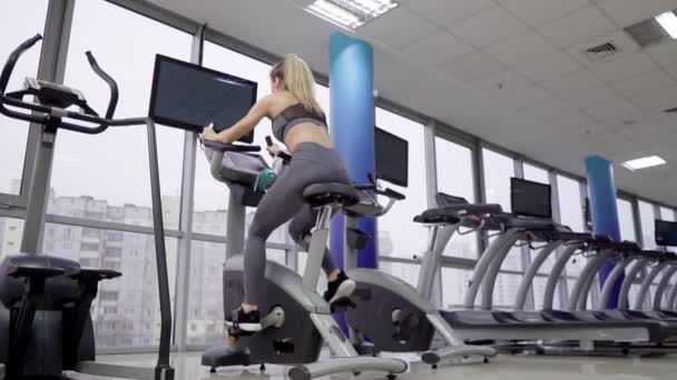 Mujer joven en bicicleta en el gimnasio haciendo ejercicio — Vídeo de stock