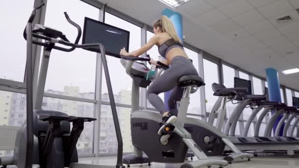 जिम व्यायाम में बाइक पर युवा महिला — स्टॉक वीडियो