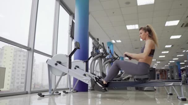 Mujer joven haciendo ejercicio en la máquina de fila en el gimnasio — Vídeo de stock