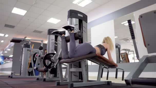 Joven mujer deportiva la construcción de los músculos de las piernas en una máquina de entrenamiento en el gimnasio — Vídeo de stock