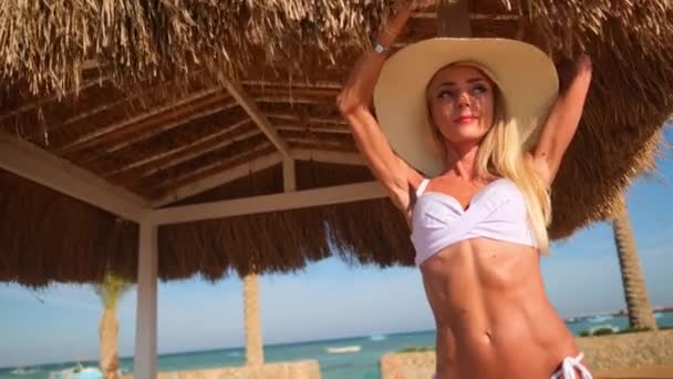 Sahilde saman tepe örtüsünün altında duran bikini giyen seksi kadın. — Stok video