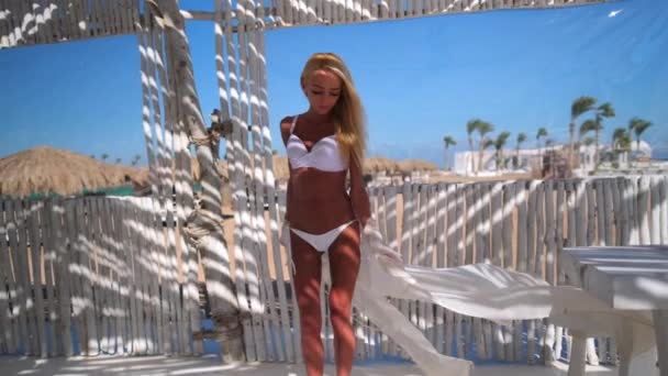 Atractiva joven mujer con traje de baño y pareo caminando en la cafetería de playa con interior de bambú blanco — Vídeos de Stock