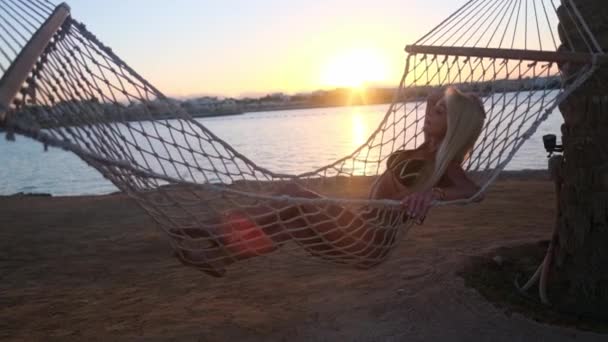 Resor och semester koncept - Kvinna avkopplande på hängmatta på stranden vid solnedgången — Stockvideo