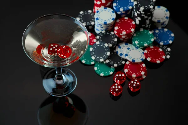 Pila de Casino fichas de juego, vaso de vermut martini y dados rojos aislados sobre fondo negro reflectante — Foto de Stock