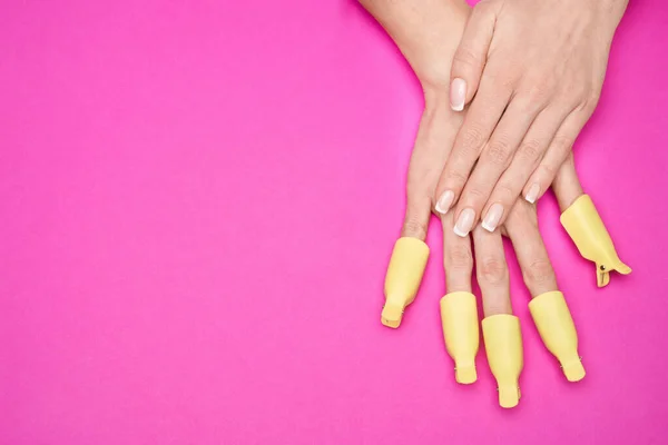 Uma mão de mulher com conjunto de mulheres de plástico prego arte mergulhar fora clipe tampa gel UV removedor de polonês wrap ferramenta para cuidados com as unhas goma-laca em casa no fundo rosa — Fotografia de Stock