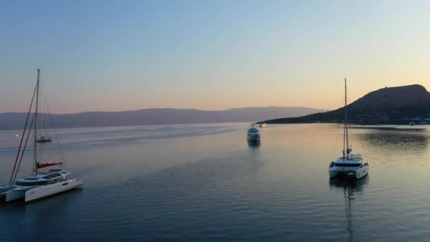 Katamaran ve yelkenli yatları güneşin doğuşunda derin mavi deniz suyunda demirli. — Stok video