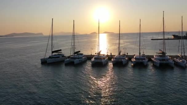 Катамаран и парусные яхты, стоящие на якоре в бухте на глубокой синей морской воде на восходе солнца — стоковое видео