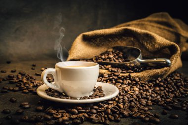 Kızarmış kahve çekirdekleriyle çevrili dumanı tüten kahve fincanı espresso.