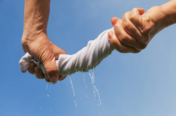 Hands squeeze wet fabric against blue sky. — Stock Photo, Image
