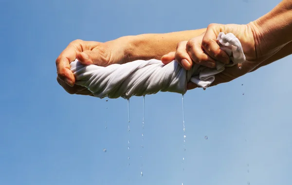 As mãos apertam o tecido molhado contra o céu azul . — Fotografia de Stock