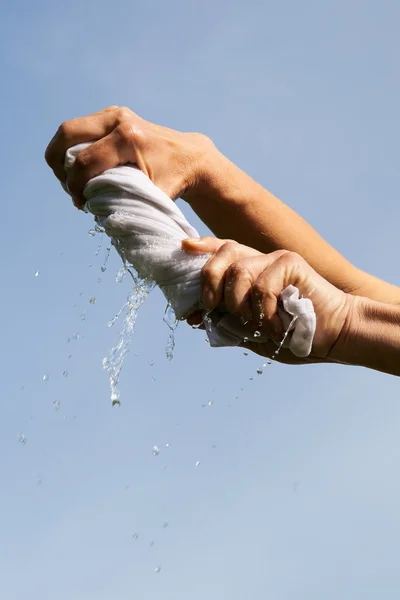 Hands squeeze wet fabric against blue sky. — Stock Photo, Image