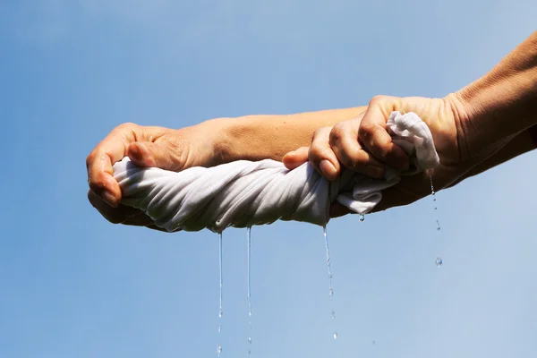 Hands squeeze wet fabric against blue sky. — Stock Photo, Image