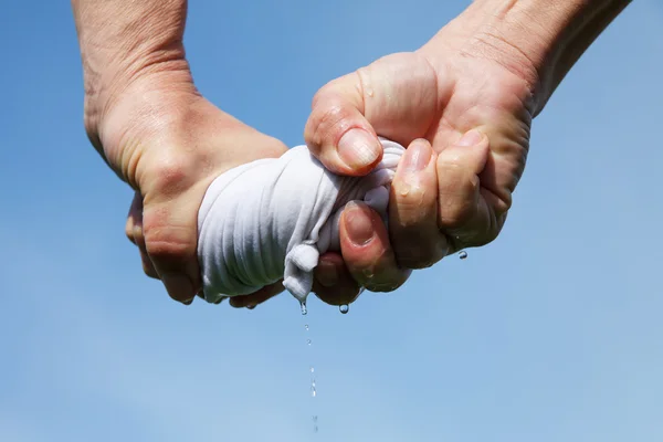 Hands squeeze wet fabric against blue sky. — Stock Photo, Image