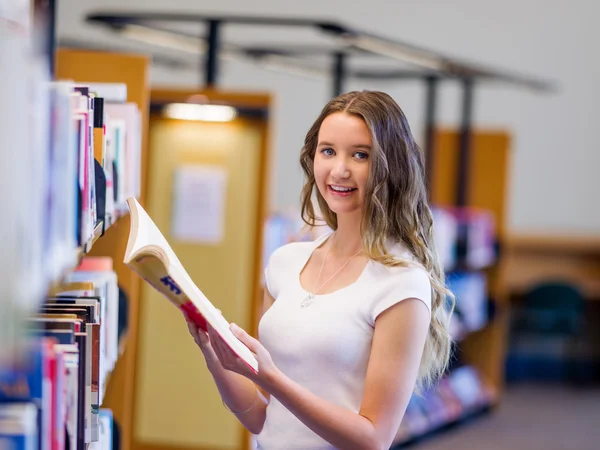Счастливая студентка забирает книги в библиотеке — стоковое фото