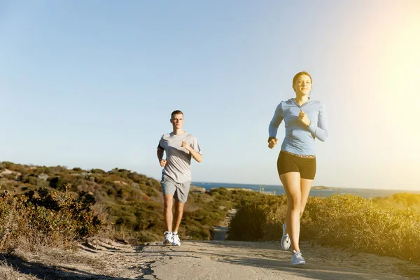 Sportlerin joggt mit ihrem Partner am Strand — Stockfoto