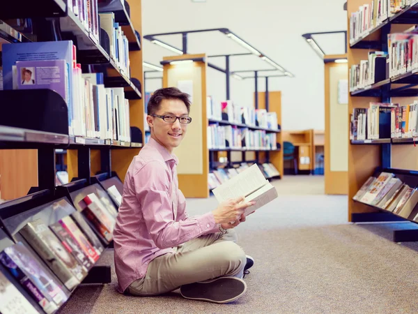 Estudante do sexo masculino feliz segurando livros na biblioteca — Fotografia de Stock