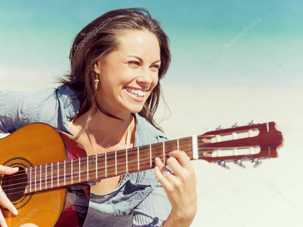 Beautiful young woman playing guitar on beach