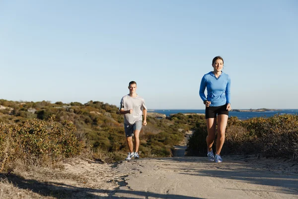 Sportlerin joggt mit ihrem Partner am Strand — Stockfoto