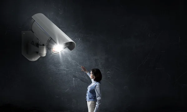 Junge Frau im Zimmer unter Kontrolle der Videokamera — Stockbild Kamera behält Frau im Auge — Stockfoto