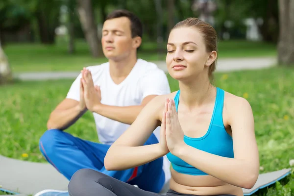 Jovem casal meditando na grama verde — Fotografia de Stock