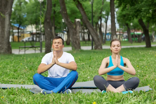 Jeune couple méditant sur l'herbe verte — Photo