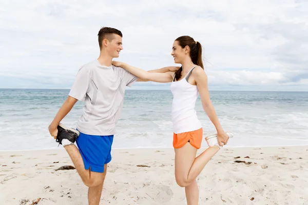 Corredores. Jovem casal exercitando e stertching na praia — Fotografia de Stock