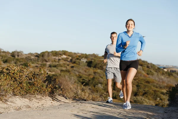 Sportlerin joggt mit ihrem Partner am Strand — Stockfoto