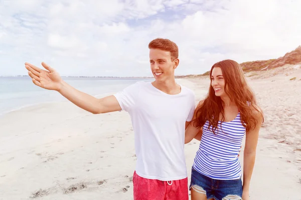 Счастливый молодой человек и женщина вместе прогуливаются по пляжу — стоковое фото