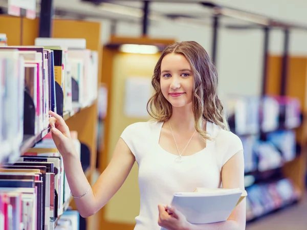 Glad kvinnlig student håller böcker på biblioteket — Stockfoto