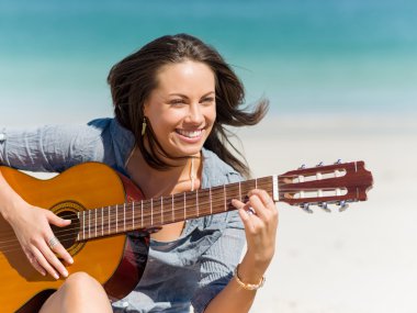 Güzel genç bir kadın sahilde gitar çalıyor.
