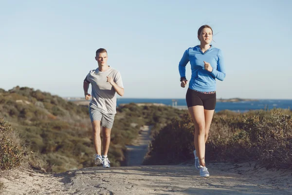 Sportlerin joggt mit ihrem Partner am Strand — Stockfoto