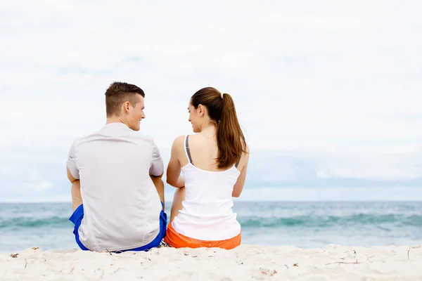 Jong paar kijken naar elkaar terwijl zitten op het strand — Stockfoto