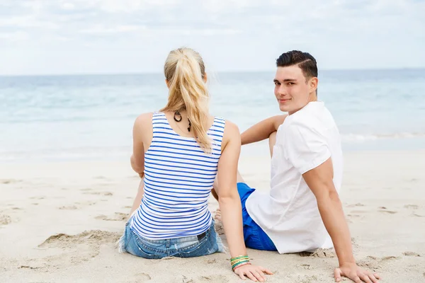 Romantiska unga paret sitter på stranden — Stockfoto