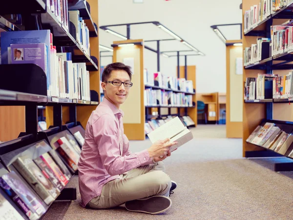 Estudante do sexo masculino feliz segurando livros na biblioteca — Fotografia de Stock