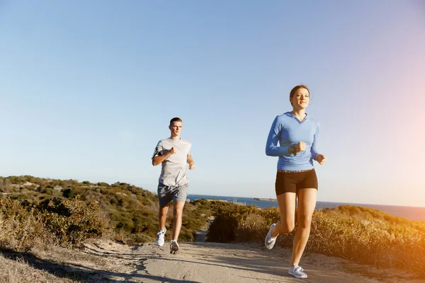 Sportlerin joggt mit ihrem Partner am Strand — Stockfoto