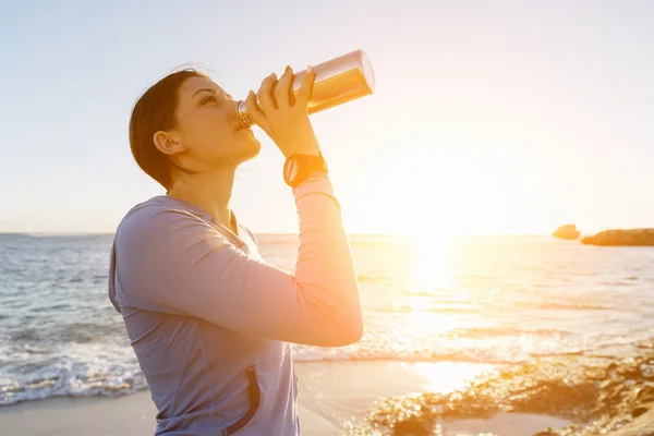 Woman drinking water on beach — Stock Photo, Image