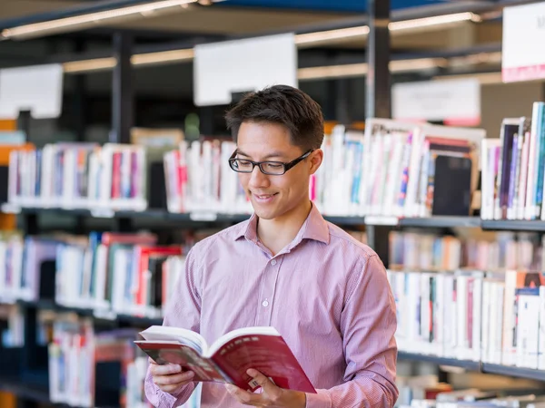 Glücklicher männlicher Student mit Büchern in der Bibliothek — Stockfoto