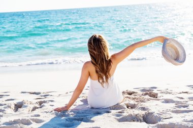 Genç bir kadın sahilde oturuyor.